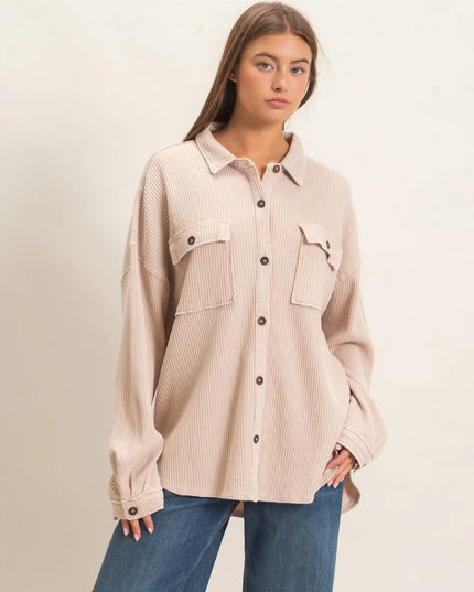 A woman modeling a light beige ribbed button-up shirt with two chest pockets, worn with blue jeans against a plain off-white background.