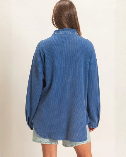 A person shown from the back wearing an oversized blue corduroy button-up shirt and light denim shorts against a plain off-white background.