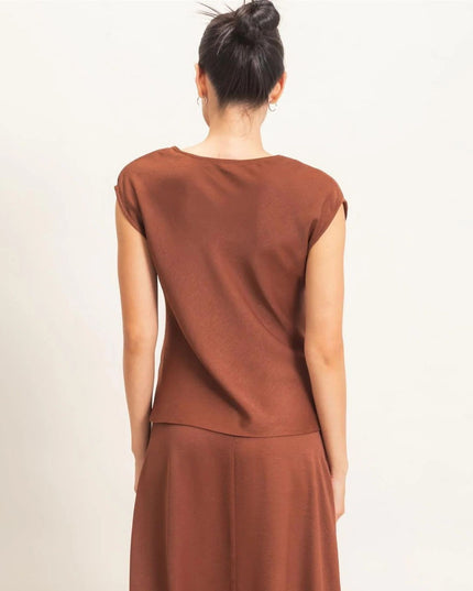 A woman viewed from behind wearing a rust-brown sleeveless top and matching skirt against a plain off-white background.