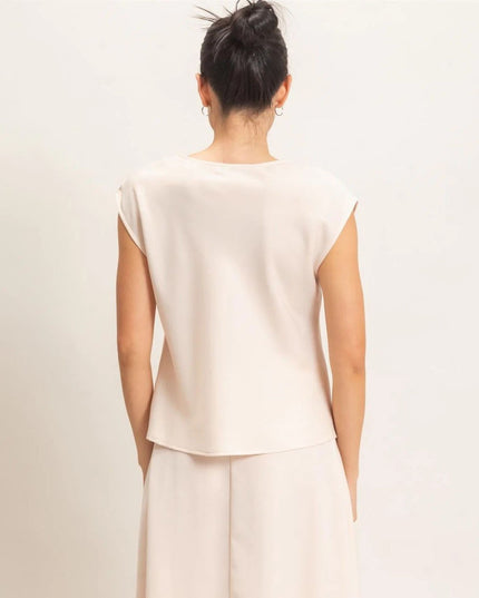 A woman viewed from behind wearing a light cream or off-white sleeveless top and matching wide-leg trousers against a plain light background.