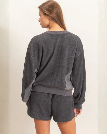 A woman shown from the back wearing a dark gray heathered sweatshirt and matching shorts against a light textured wall.