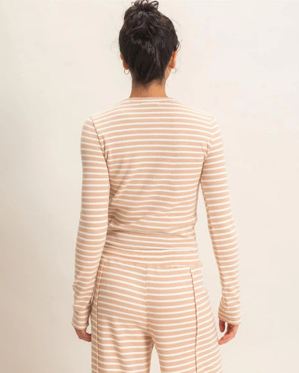 A woman viewed from behind wearing a beige and white striped long-sleeve top and matching striped pants against a plain light beige studio background.