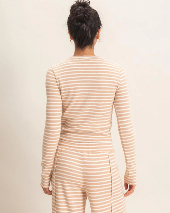 A woman viewed from behind wearing a beige and white striped long-sleeve top and matching striped pants against a plain light beige studio background.