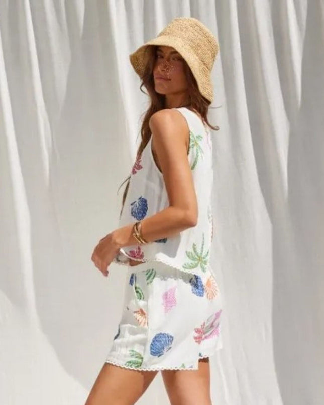 Woman wearing a white dress with colorful floral patterns and a straw hat against a white curtain background.