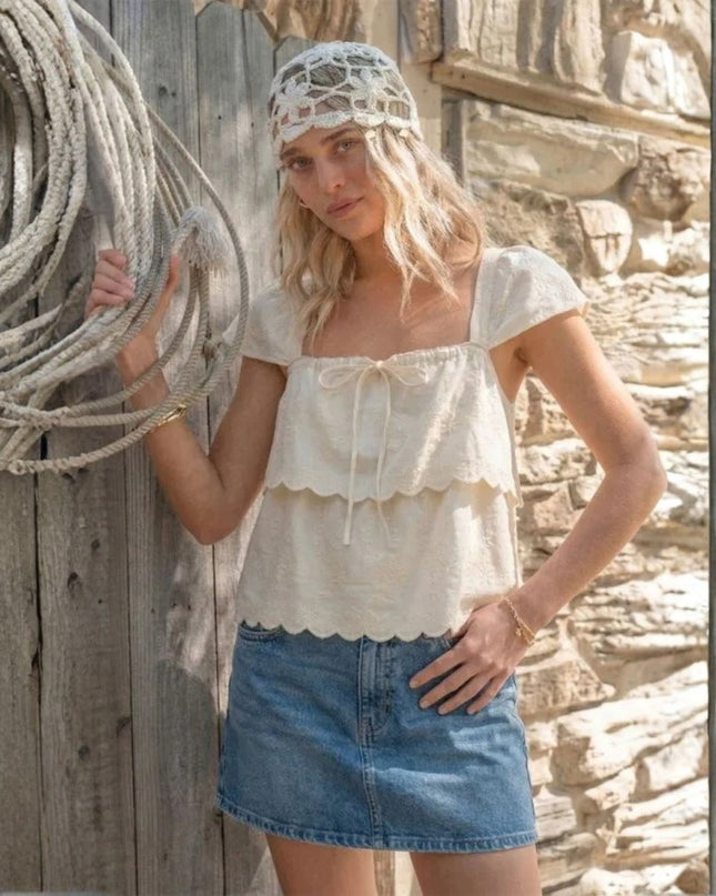 Woman in a white top and denim skirt standing next to a wooden wall with rope.