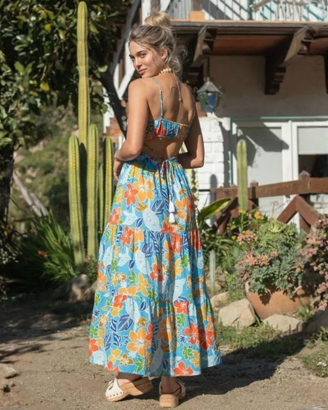 Woman wearing a colorful floral dress standing outdoors with plants and a house in the background
