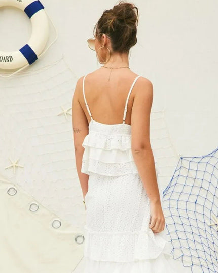 A woman viewed from behind wearing a white ruffled spaghetti-strap dress, standing against a nautical-themed wall with a life preserver, netting, and starfish.