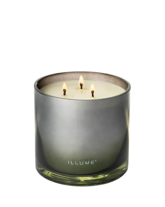 Three-wick candle in a green glass container with 'ILLUME' branding on a white background