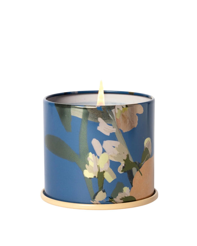 Candle in a blue container with floral design on a white background