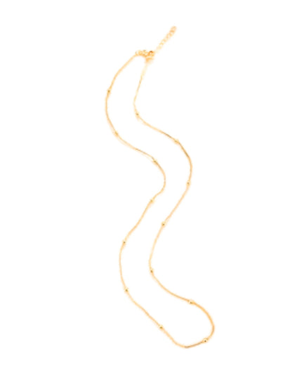 A delicate gold chain necklace with small spaced beads, displayed in a wavy S-shape on a solid white background.