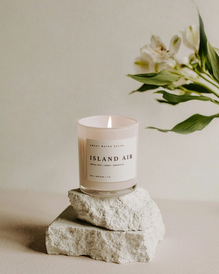 Candle labeled 'Island Air' on a rock with a flower in the background