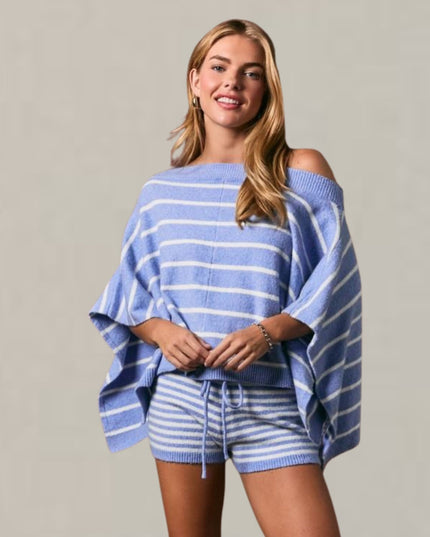 A woman modeling a light blue and white striped knit two-piece set featuring an off-the-shoulder poncho-style top and matching drawstring shorts, set against a plain light gray studio background.