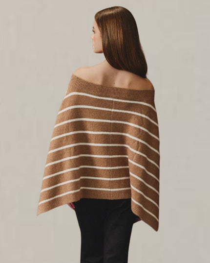 A woman shown from the back wearing a brown knit poncho-style sweater with thin white horizontal stripes, paired with black pants, against a plain light gray studio background.