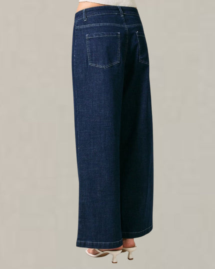 A pair of dark blue wide-leg denim jeans shown from the back, worn by a model with white heeled sandals against a plain light gray background.