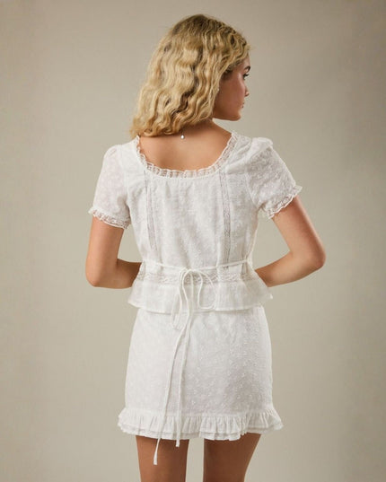 Woman wearing a white lace dress against a beige background