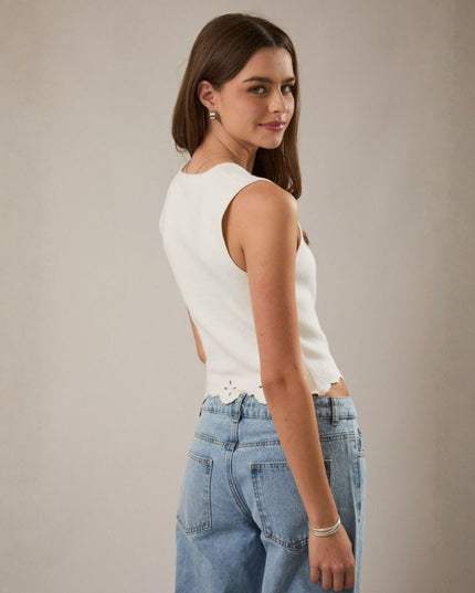 Woman wearing a white sleeveless top and blue jeans against a plain background