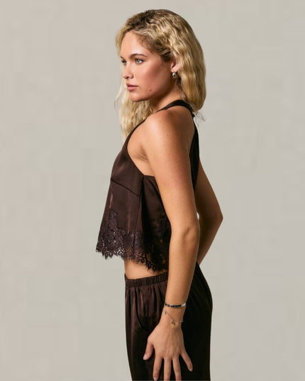A woman in side profile wearing a dark brown sleeveless top with lace trim and matching dark brown pants, photographed against a plain light gray studio background.