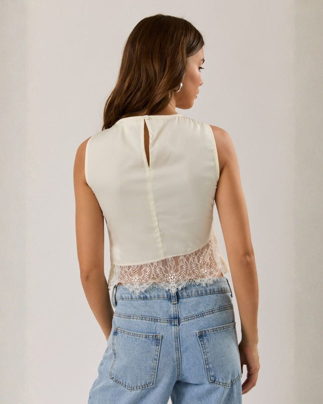 Woman wearing a white sleeveless top with lace detail and light blue jeans against a plain background