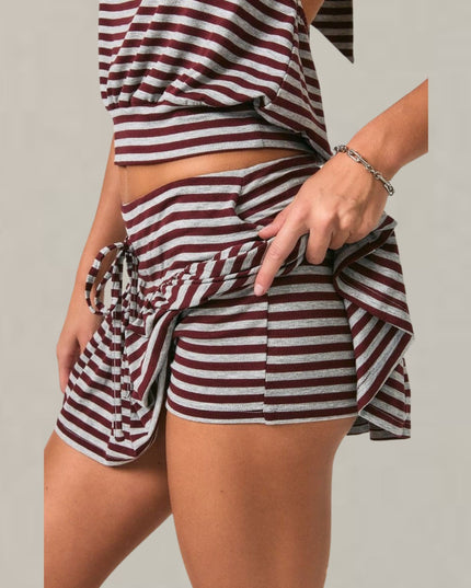 A close-up of a person wearing a matching two-piece set with horizontal burgundy and off-white stripes. The set includes a cropped top and ruffled shorts with a side tie detail, shown against a plain light gray background.