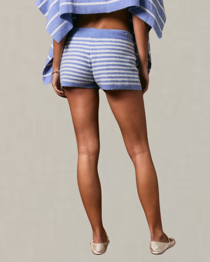 A model from behind wearing blue and white striped knit shorts and a matching striped knit top, paired with beige flat shoes, against a solid light gray background.
