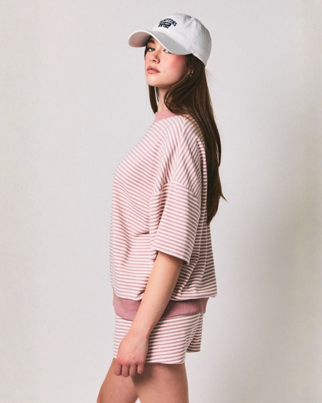 Woman wearing a pink striped outfit and white cap against a plain background