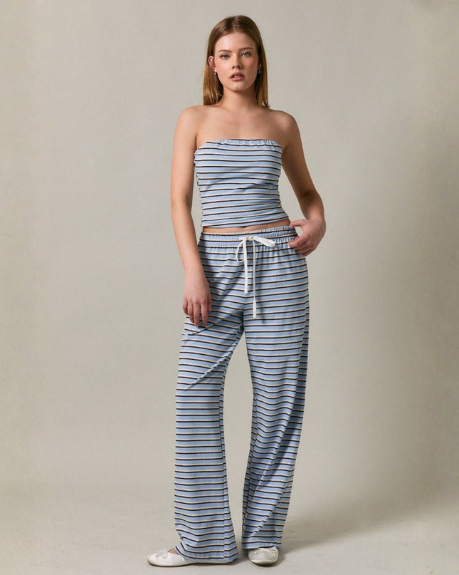Woman wearing a striped strapless top and wide-leg pants on a plain background