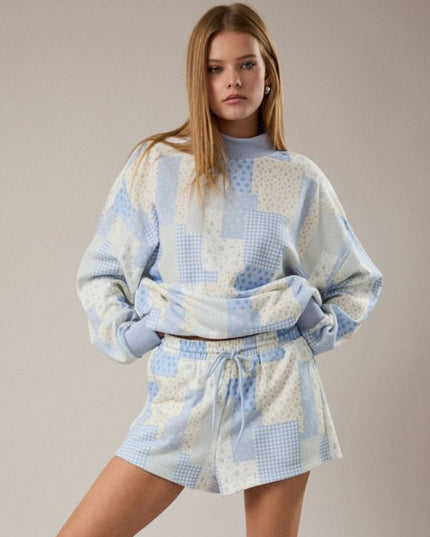 Woman wearing a patchwork-style outfit with a sweater and shorts on a plain background