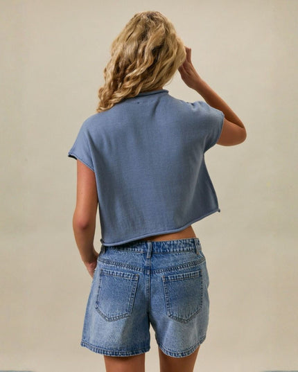 Person wearing a blue crop top and denim shorts against a beige background
