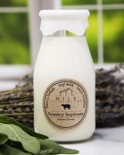 Milk bottle-shaped candle labeled 'Milk Barn Candles' with lavender and sage in the background