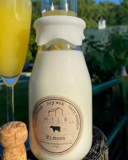 Milk bottle labeled 'Mimosa' with a glass of orange juice and a cork, outdoors.