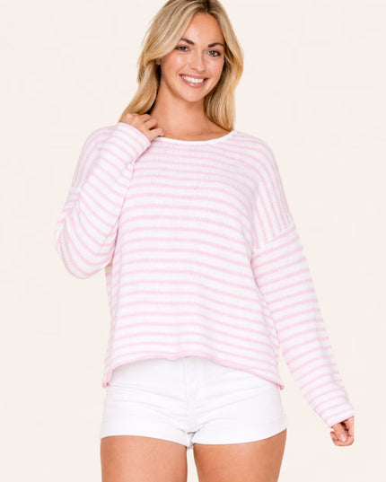 Woman wearing a pink and white striped sweater and white shorts on a beige background