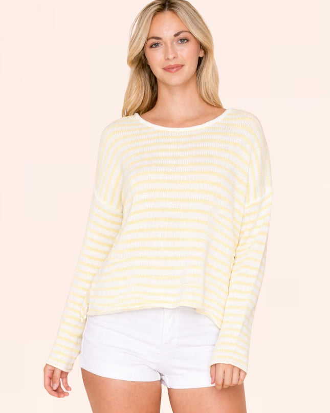 Woman wearing a yellow and white striped sweater with white shorts on a beige background