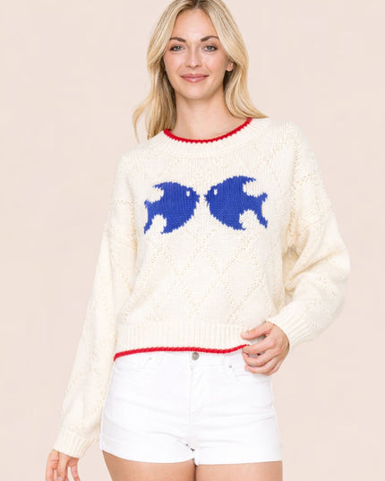 Woman wearing a cream sweater with blue fish designs on a beige background