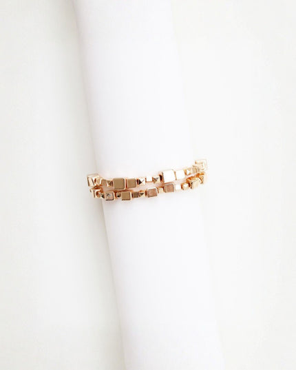 A rose gold cube-link ring displayed on a white cylindrical ring stand against a clean white background.