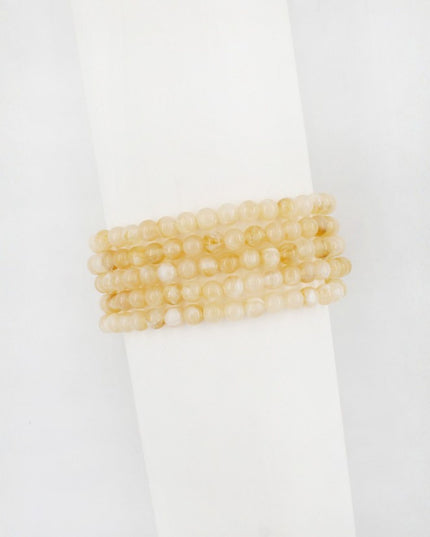 A stack of four beaded stretch bracelets in a pale, translucent yellow-gold color, displayed on a white cylindrical stand against a white background.
