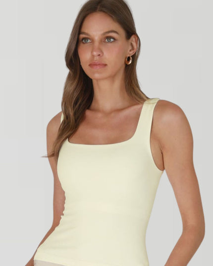 Woman wearing a light yellow sleeveless top against a plain background