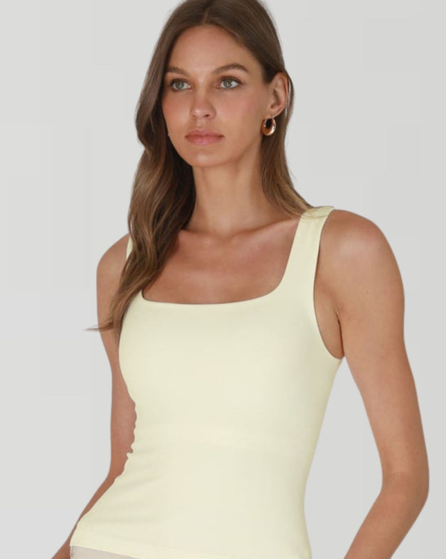Woman wearing a light yellow sleeveless top against a plain background