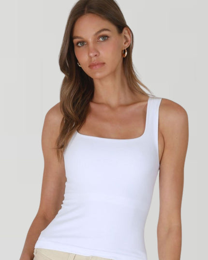 Woman wearing a white tank top against a plain background