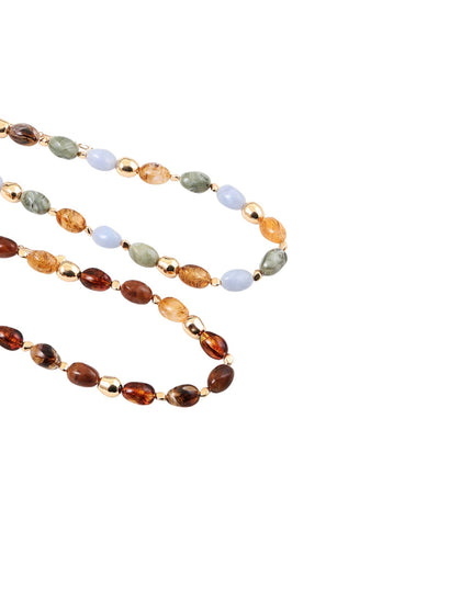 A beaded strand necklace with alternating oval brown amber-like beads, light blue stone beads, olive green stone beads, and small metallic gold spacer beads, arranged on a plain white background.