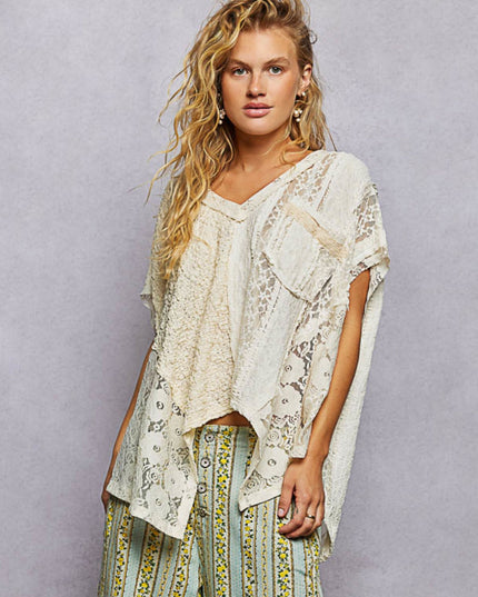 A woman modeling a bohemian-style cream lace and crochet top with matching patterned pants against a textured gray studio background.