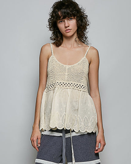 A woman modeling a cream-colored crochet and lace camisole top with thin straps and a scalloped hem, paired with gray shorts, against a solid gray studio background.