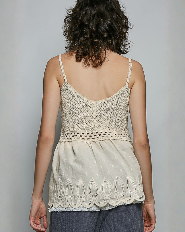 A woman shown from the back wearing a cream-colored crochet camisole top with thin straps and a scalloped lace hem, paired with dark gray pants, against a plain light gray background.
