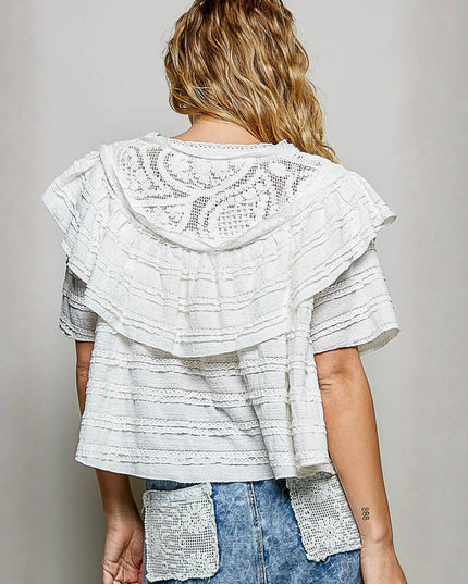 A woman shown from the back wearing a white tiered ruffle top with a lace-embroidered hood and denim shorts with sequined pockets, set against a plain gray studio background.