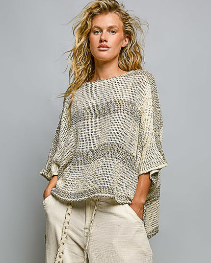 A woman modeling a loose, open-knit cropped sweater with wide three-quarter sleeves in a textured cream and gray striped pattern, paired with light beige pants, against a solid gray studio background.