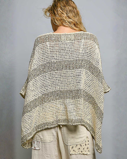 A woman shown from the back wearing a loose, open-knit striped poncho or shawl in cream and taupe-beige tones, paired with light beige pants, against a plain gray studio background.