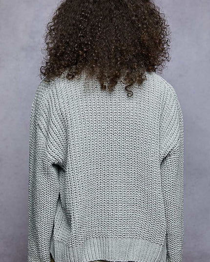 A person shown from the back wearing a chunky knit light gray sweater, with dark curly hair visible against a textured gray studio background.