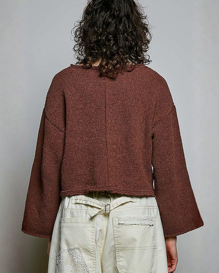A person shown from the back wearing a cropped, long-sleeve textured knit sweater in a muted reddish-brown color, paired with cream-colored pants, against a plain light gray background.