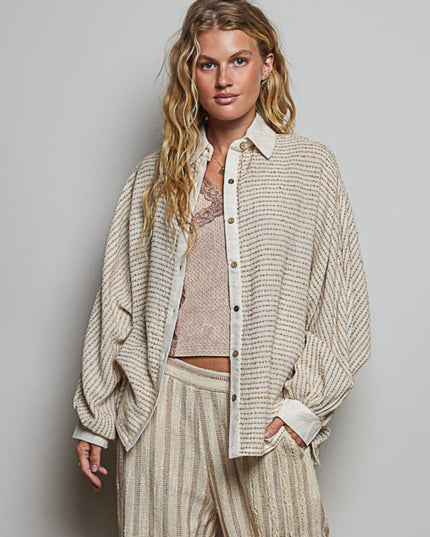 A woman modeling a textured, oversized cream and beige striped button-up shirt with matching striped trousers, layered over a lace-trimmed camisole, against a solid light gray studio background.