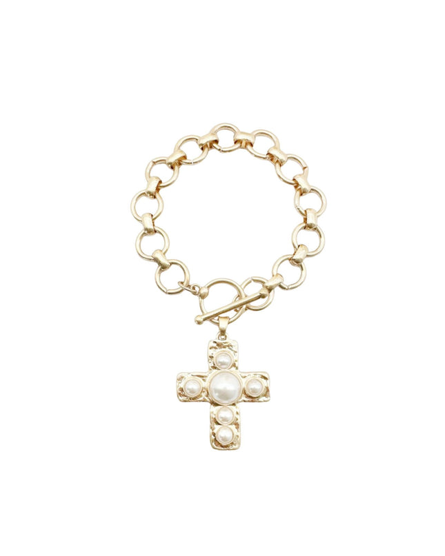 A gold chain bracelet with a toggle clasp and a dangling cross pendant adorned with white pearls, shown on a plain white background.