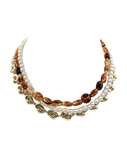 A multi-strand statement necklace featuring white faux pearls, translucent amber glass beads, and gold-toned floral charms, displayed on a clean white background.